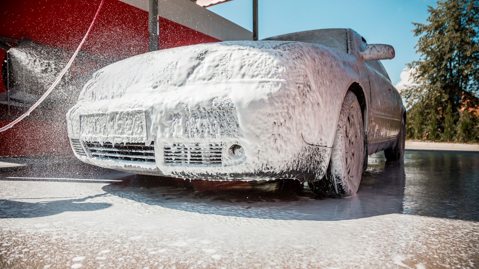 Car Covered in Foam at Outdoor Car Wash Under Clear Blue Sky