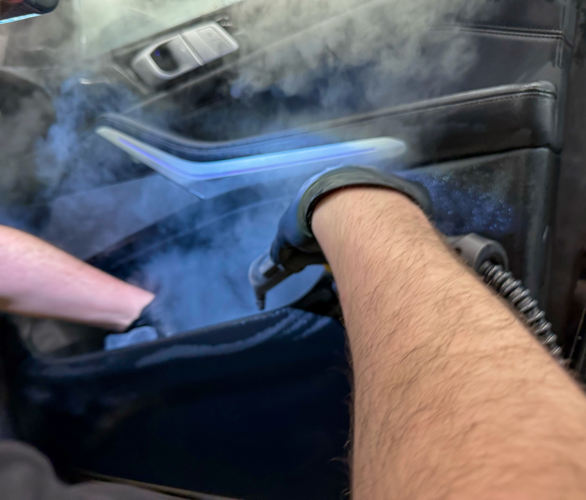 The detailing master cleans the car interior with a hot steam cleaner close-up. Car detailing and the concept of car interior care. Dry cleaning of the car interior, close-up.